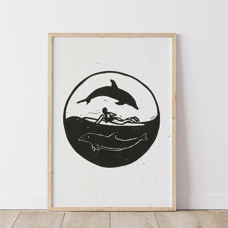 Framed artwork with black silhouette of a person surfing and dolphins in a yin and yang composition