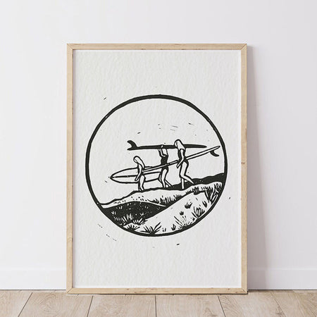 Framed artwork of three people carrying surfboards through sand dunes to the beach
