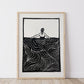 Framed black and white lino print artwork of a person swimming / wading in water on a white wall.