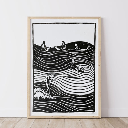 Framed black and white lino print artwork of many women surfing in the ocean together